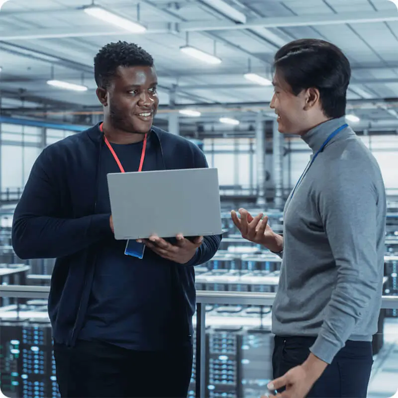 Two IT professionals smiling and talking with one holding a laptop.